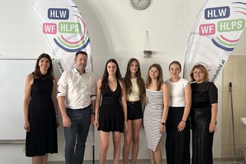 Schülerinnen der HLW Pinkafeld mit Lehrkräften und einem Vortragenden des Entrepreneurship Day zwischen zwei Beachflags der Schule